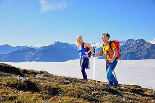 Pärchen wandert über den grünen Berg oberhalb der Wolkendecke bei strahlendem blauen Himmel