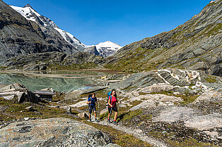 Ein Päarchen entfernt sich vom Bergsee über den felsigen und steinigen  Untergrund