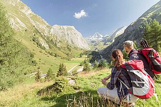 Päarchen sitzt auf einem kleinen Hügel und betrachtet das grüne tal das sich vor ihnen zwischen den Bergegn hindurchschlängelt