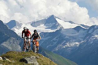 2 junge Mountainbiker fahren über den grünen Kamm am Berg- im Hintergrund erstrecken sich weitere berge