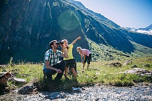 Mama, Papa Tochter und Hund rasten am Flussbett im Tal- Die Tochter deutet in die Ferne und Papa schaut durch fernglas dorthin