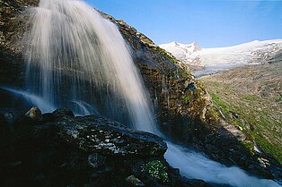 Nahaufnahme des Wasserfalls, bevor er ins Flussbeet kracht- Felsen und Bergpanorama im Hintergrund