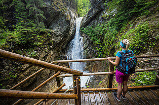 Junge Dame steh auf einer Holzplattform in der Klamm und bewundert den Wasserfall und die Schluch
