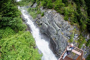 älterer Mann steht fotografierend auf einer Plattform und bewundert den Ausblick in die Schlucht und den wilden Fluss der sich den Weg in Tal bahnt